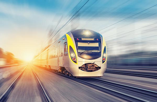 A modern high-speed train travels rapidly along railroad tracks, with a bright sunset in the background. The train's sleek design and motion blur emphasize its fast speed, fitting perfectly on a website's homepage. The scene conveys a sense of efficiency and progress.