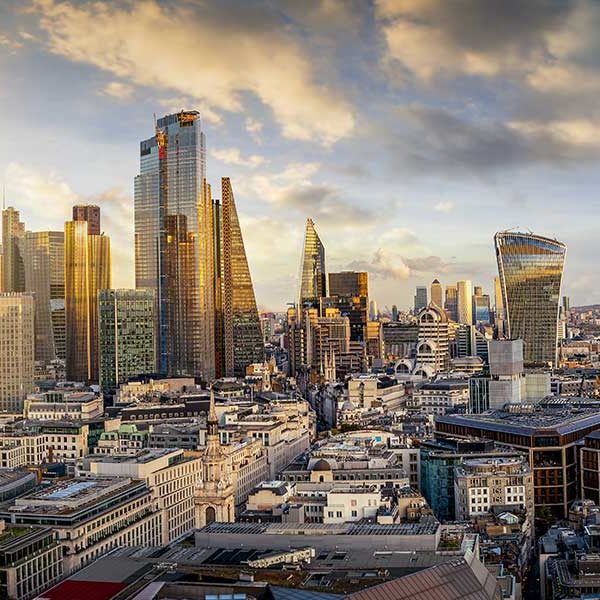 A panoramic view of a bustling cityscape at sunset, featuring numerous modern skyscrapers and buildings with diverse architectural styles, highlights the fruits of recent construction and investment plans. The partly cloudy sky, tinged with a golden hue from the setting sun, casts a warm light over the urban landscape.