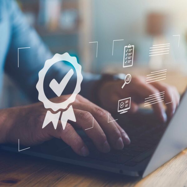Close-up of a person typing on a laptop, with transparent graphics overlayed. A badge with a checkmark, a clipboard, and a magnifying glass symbolize certification, quality assurance through ISO standards, and research. Warm lighting and blurred background enhance the professional atmosphere.