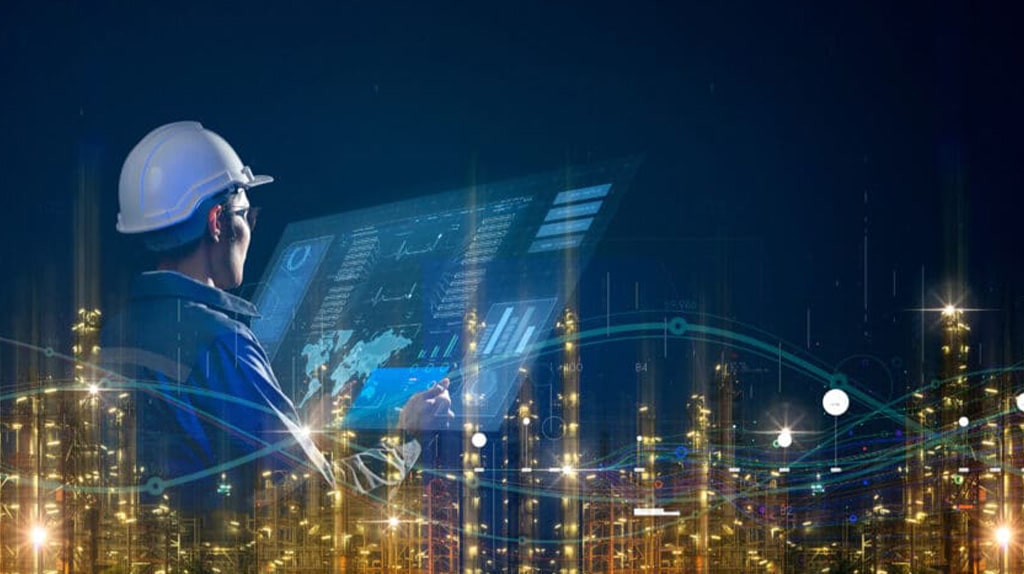 A worker wearing a white hard hat operates a large touch screen interface with AI-driven data and analytics, amidst a backdrop of illuminated industrial machinery and equipment at night. The scene blends advanced technology and industry solutions seamlessly.